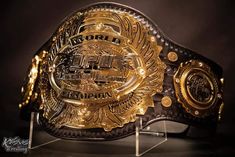 a gold and black wrestling belt sitting on top of a glass stand in front of a dark background