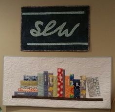 there is a quilt on the wall next to a shelf with some books and scissors