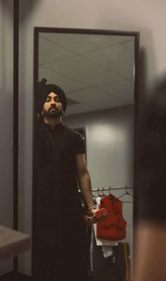 a man standing in front of a mirror looking at his reflection wearing a turban