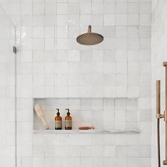 a white tiled bathroom with shower head, soap and lotion bottles on the shelf