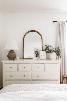 a bedroom with white furniture and a large mirror on top of the dresser next to it