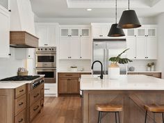 a kitchen with wooden floors and white cabinets, two pendant lights over the stove top