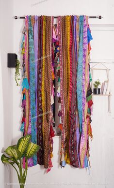 the colorful scarfs are hanging on the wall next to a potted green plant