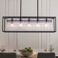 a chandelier hanging over a dining room table with wine glasses and fruit on it