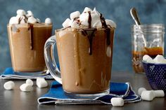 two mugs filled with hot chocolate and marshmallows on top of a table