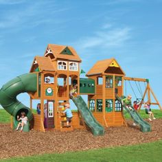 children playing on a wooden playset with green slide and climbing equipment in the grass