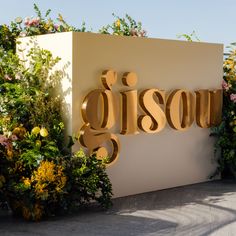 a sign that says gibson surrounded by plants and flowers in front of a white wall