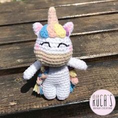 a crocheted stuffed animal unicorn sitting on top of a wooden bench with its eyes closed