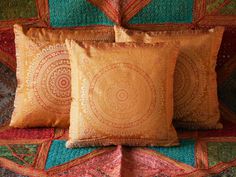 three decorative pillows on a quilted bedspread, one in gold and the other in green