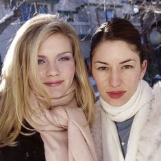 two women standing next to each other in front of snow covered trees and buildings,