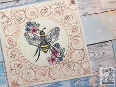 a card with a bee and flowers in the center on a wooden surface, surrounded by wood planks