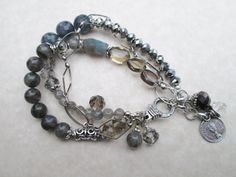 "This silver-toned, three-stranded bracelet is made of faceted dark blue Aquamarine, green Labradorite, light blue Labradorite, Smoky Quartz and Swarovski crystals.  A dainty chain, small silver coin and lobster claw clasp complete the piece.  The bracelet measures 7.5\" extendable to 8\" with existing chain extension." Silver Double Strand Bohemian Bracelets, Bohemian Double Strand Silver Bracelets, Bohemian Silver Faceted Beaded Bracelets, Silver Multi-strand Spiritual Bracelets, Spiritual Silver Multi-strand Bracelets, Spiritual Multi-strand Silver Bracelets, Silver Double Strand Bracelets With Gemstone Beads, Silver Multi-strand Bracelet With Gemstone Beads, Silver Double Strand Bracelet With Natural Stones