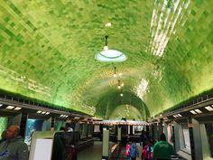 people are walking through an underground subway station with green tiles on the walls and ceiling