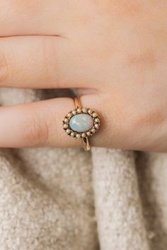 a woman's hand wearing a gold ring with an opal stone in the center