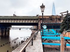 blue benches along the side of a river with a bridge in the background