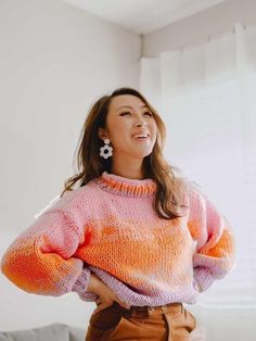 a woman in an orange and pink sweater smiles while standing next to a white couch