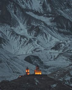 the mountains are covered in snow and there is a small church lit up at night