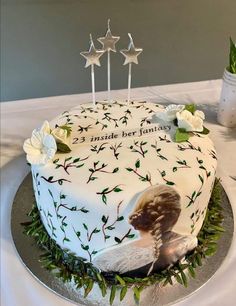 a white cake with green leaves and flowers on it, sitting on a silver platter