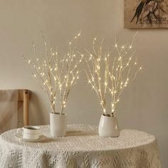 two white vases filled with branches on top of a table