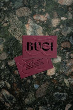 two red business cards sitting on top of a green marble surface with the word buch printed on it