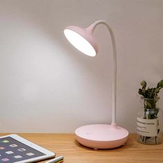 a pink lamp sitting on top of a wooden table next to a tablet computer and potted plant