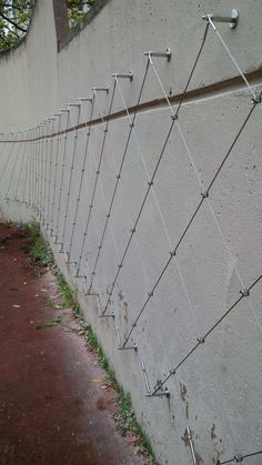 a wall that has some wires attached to it and is next to a sidewalk with grass growing on the ground