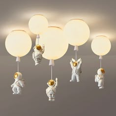 an astronaut themed ceiling light fixture with five lights attached to it, and three astronauts hanging from the ceiling