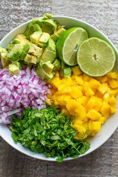 a white bowl filled with chopped up vegetables and limes next to sliced avocado