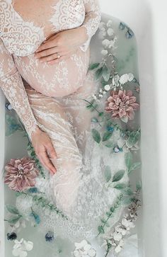 a pregnant woman laying in a bathtub with flowers on the side and her stomach exposed