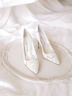 two pairs of white wedding shoes sitting on top of a round tray in the middle of a bed