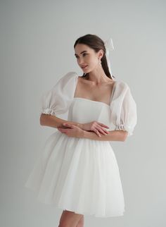 a woman is wearing a white dress with sheer sleeves and a bow in her hair