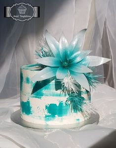 a white and blue cake with a flower on the top is sitting on a table