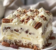 a piece of cake with white frosting and pecans on top sitting on a plate