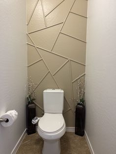 a white toilet sitting in a bathroom next to two black vases with flowers on them