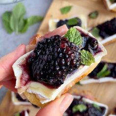 a person is holding up a pastry with berries on it and mint leaves around the edges