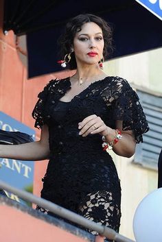 a woman in a black dress holding an umbrella and looking off to the side with her hand on her hip