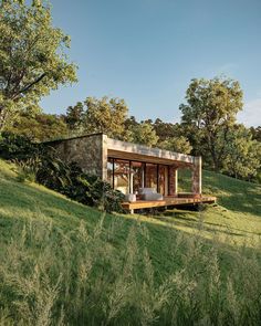 a small house sitting on top of a lush green hillside next to trees and grass