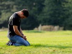 a man sitting in the grass with his hands on his knees looking down at something