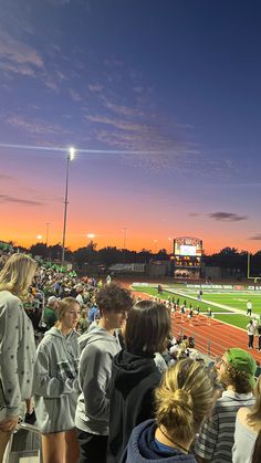 a group of people standing on top of a soccer field at sunset with the sun going down