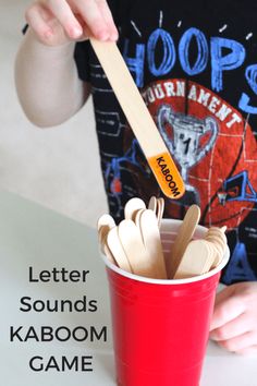 a young boy is playing with wooden spoons in a red cup that says letter sounds kaboom game