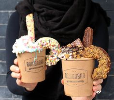 two people holding up cups with donuts and sprinkles