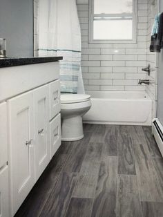 a white bathroom with wood flooring and gray tile on the walls, along with a bathtub