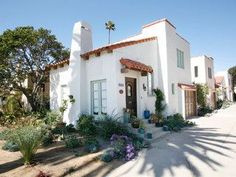 a white house with palm trees and flowers in the front yard on a sunny day