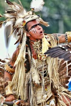 a native american man with feathers on his head and hands, holding something in one hand