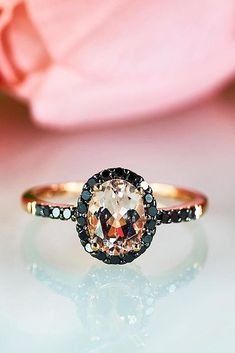 an orange and black diamond ring sitting on top of a table next to a pink rose