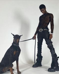 a man in black clothes holding a leash with a dog sitting next to him on a white background