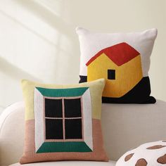 two pillows sitting on top of a white couch next to a pillow shaped like a house