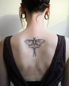 the back of a woman's neck with a small moth tattoo on her left shoulder