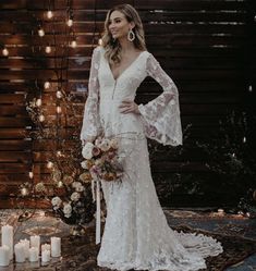 a woman standing in front of candles wearing a wedding dress with long sleeves and bell sleeves