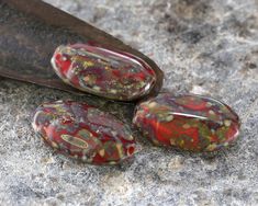 three red and green rocks sitting on top of a rock next to a metal knife